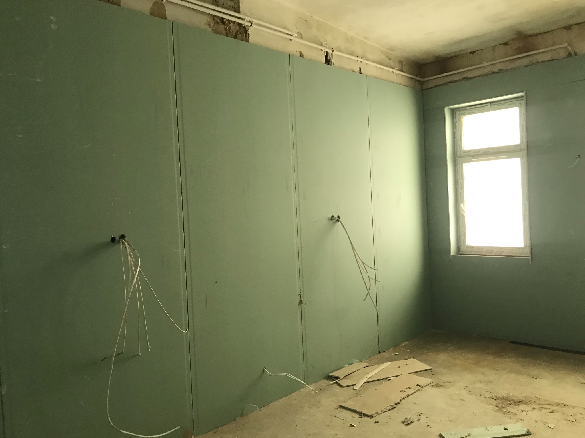 Montaż płyt gipsowo-kartonowych na ścianach w pomieszczeniu z wyprowadzonymi przewodami elektrycznymi i widocznymi niedoskonałościami sufitu.