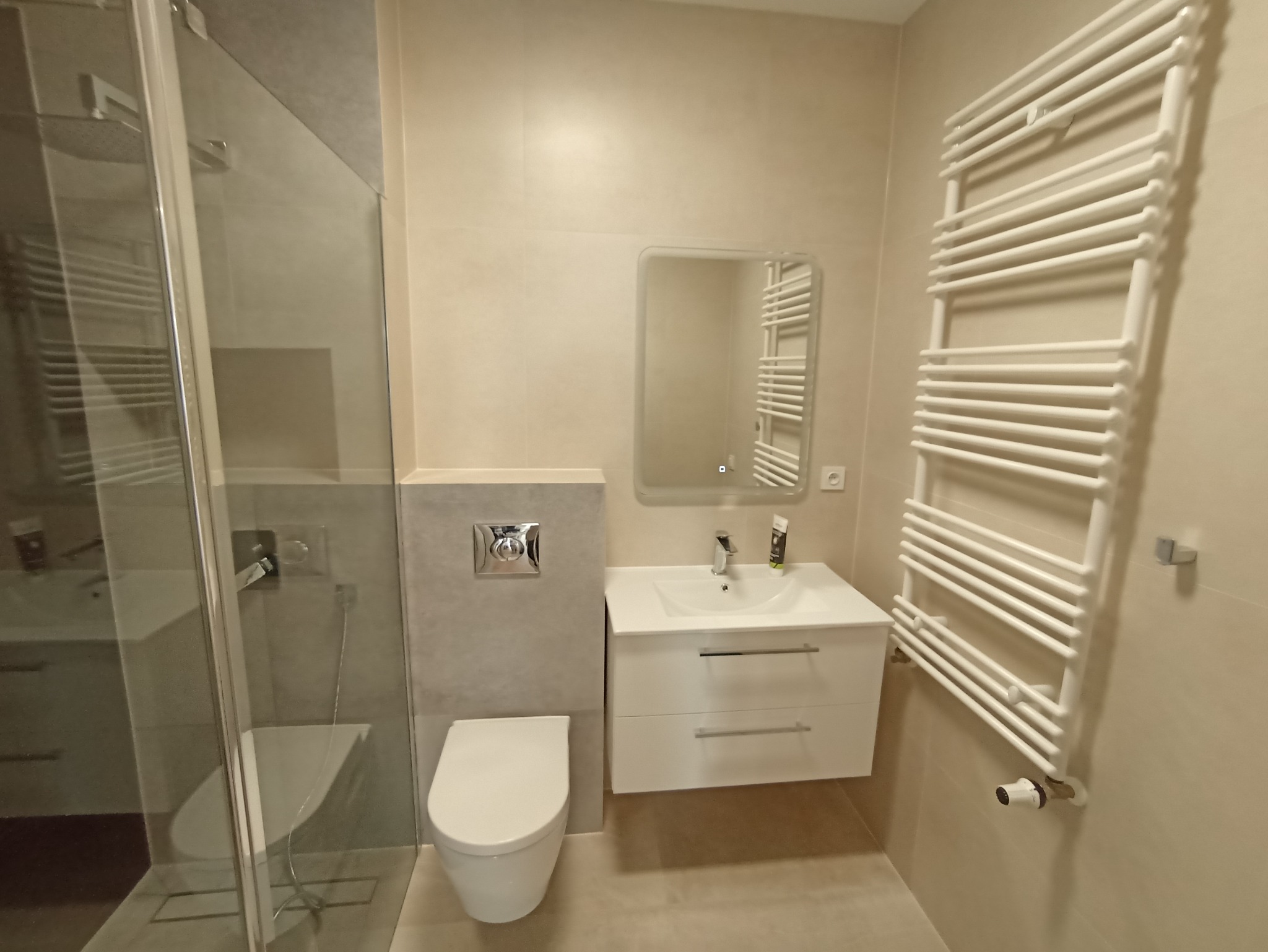 Jasna łazienka w Szczecinie z kabiną prysznicową, podwieszaną toaletą, umywalką z szafką i białym grzejnikiem drabinkowym.