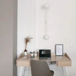 Jasne biurko z laptopem, lampą kulkową i dekoracjami w minimalistycznym wnętrzu z panelami ściennymi.