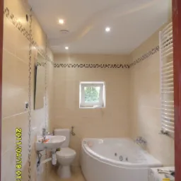 Jasna łazienka po remoncie z narożną wanną z hydromasażem, beżowymi płytkami z dekoracyjnym paskiem i podwieszanym sufitem z oświetleniem punktowym.