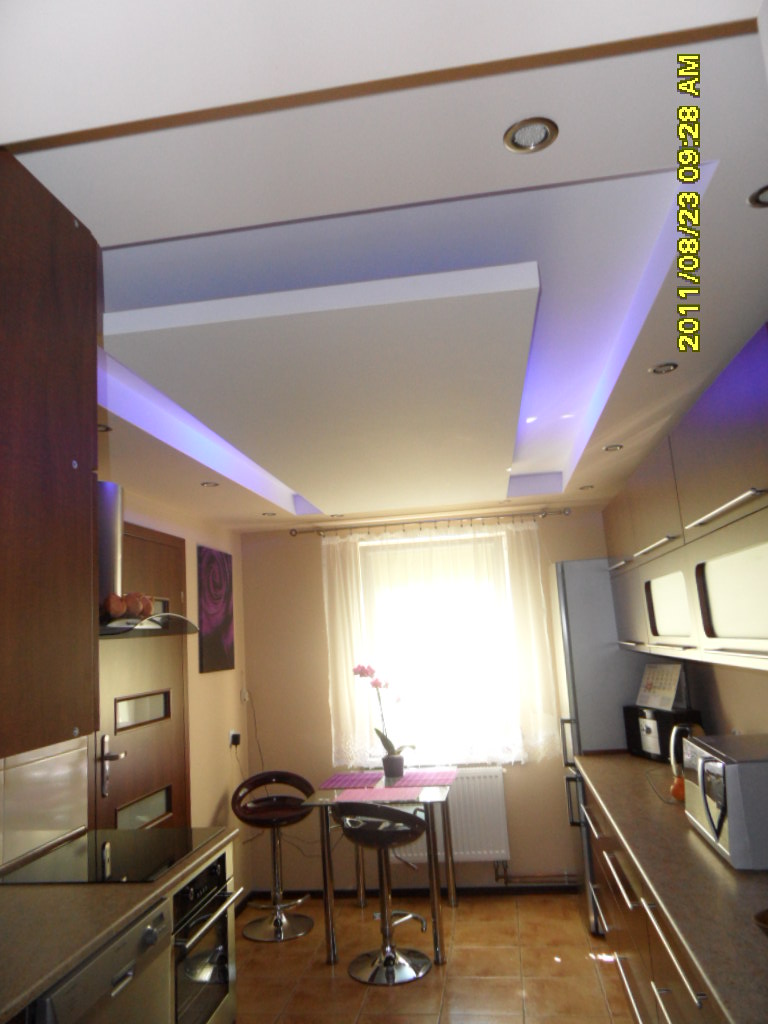 Kuchnia z podwieszanym sufitem z oświetleniem LED, widoczne zabudowy KG i nowoczesne meble kuchenne.