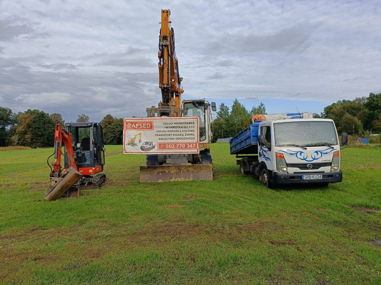 Dwie koparki (mini i kołowa) oraz wywrotka na trawiastym terenie. Na większej koparce baner firmy RAFSED z ofertą usług minikoparką, transportu kruszyw i numerem telefonu.