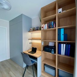 Vaker Paweł Głownicki - Pokój z szarą szafą na wymiar, biurkiem z oświetleniem i regałem z jasnego drewna z książkami i segregatorami.