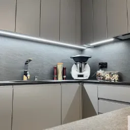 Nowoczesna kuchnia w odcieniach szarości z oświetleniem LED podszafkowym, minimalistycznym zlewem i baterią, oraz dekoracyjnymi słoikami z zawartością na blacie.