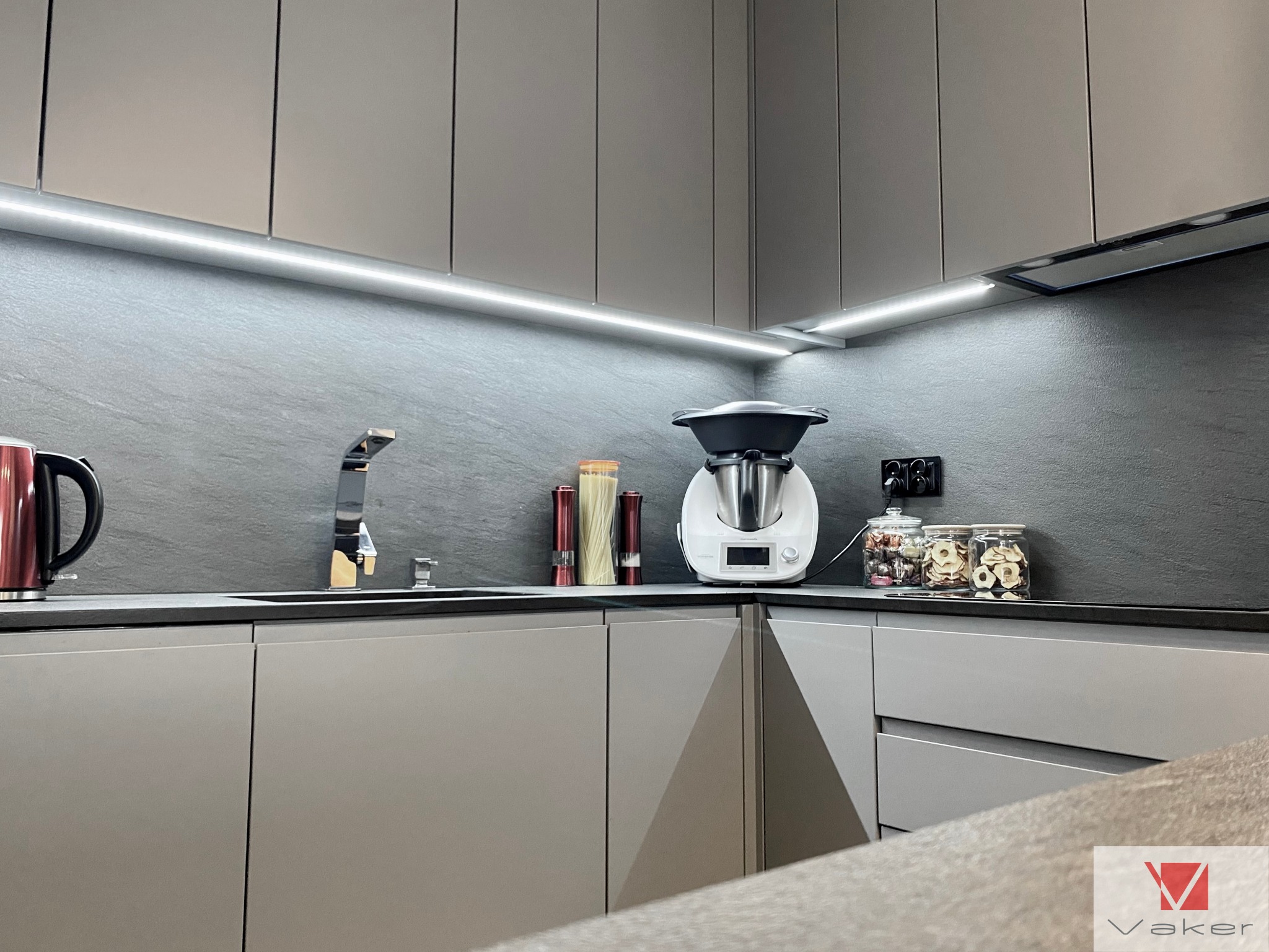 Nowoczesna kuchnia w odcieniach szarości z oświetleniem LED podszafkowym, minimalistycznym zlewem i baterią, oraz dekoracyjnymi słoikami z zawartością na blacie.