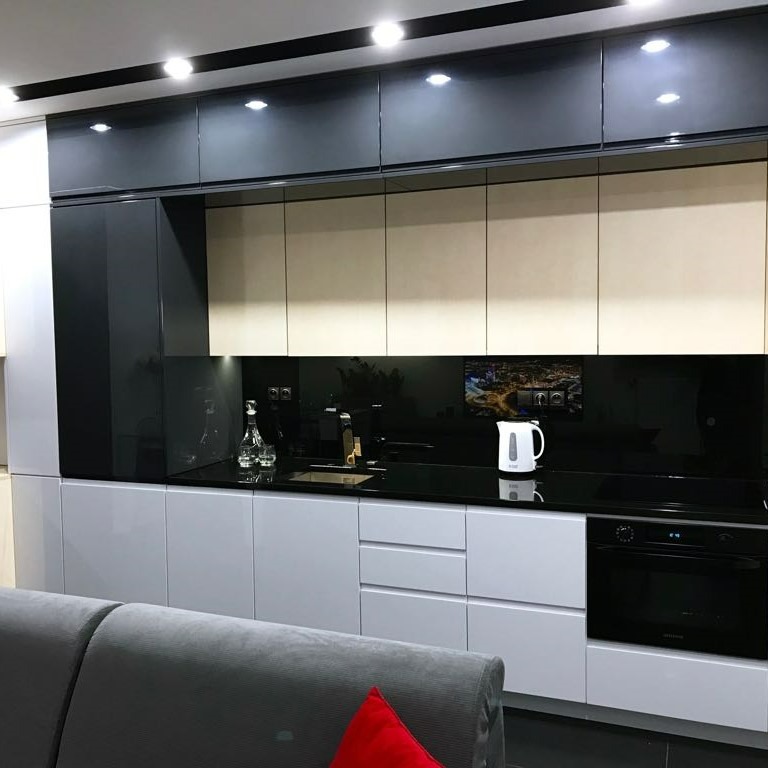 Nowoczesna kuchnia z białymi, szarymi i czarnymi frontami szafek, czarnym blatem, szklanym panelem nad blatem z widokiem miasta i oświetleniem punktowym, widziana z perspektywy salonu.