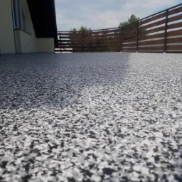 Szara posadzka z żywicy epoksydowej z dekoracyjnymi płatkami na balkonie z drewnianą balustradą, widok z niskiej perspektywy.