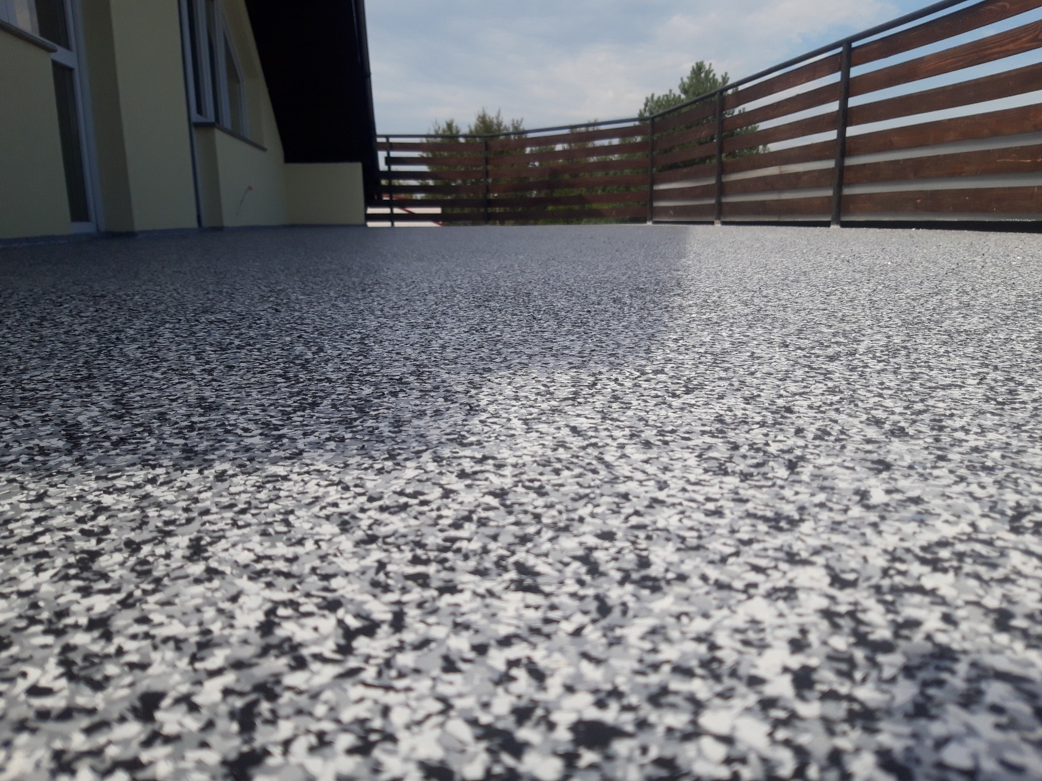 Szara posadzka z żywicy epoksydowej z dekoracyjnymi płatkami na balkonie z drewnianą balustradą, widok z niskiej perspektywy.