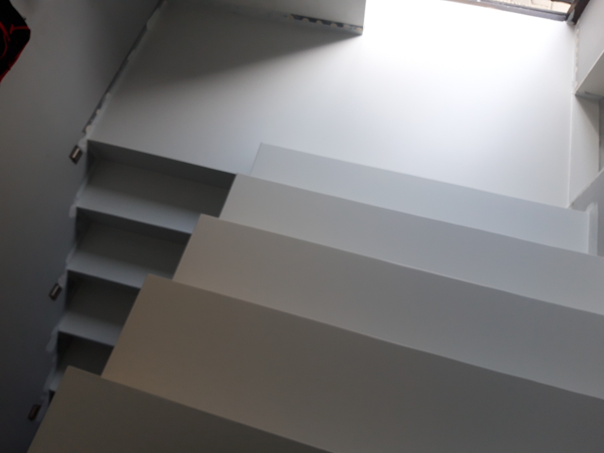 Minimalistyczne, białe schody z widocznymi stopniami i boczną ścianą. Ujęcie z dołu, podkreślające geometrię i czystość formy. Górne światło naturalne.