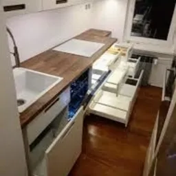 Nowoczesna kuchnia z drewnianym blatem, białymi szafkami i wysuwanymi półkami, widziana z góry, z otwartymi szufladami i oświetleniem LED w lodówce na wino.