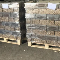 Dwa palety z brykietem drzewnym owinięte folią stretch, widoczne etykiety z informacjami o wadze na wierzchu palet.