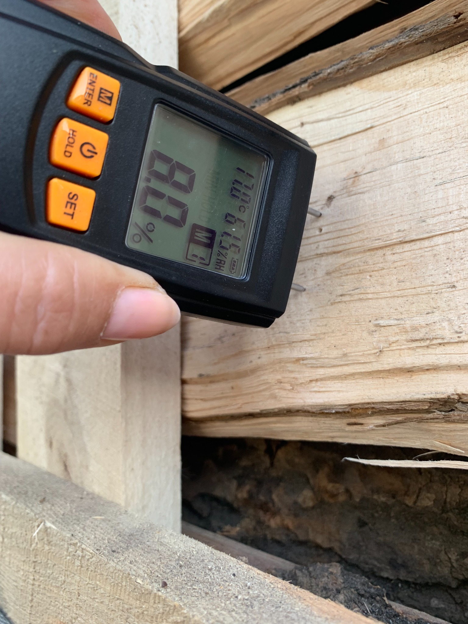 Pomiar wilgotności drewna kominkowego za pomocą wilgotnościomierza elektronicznego, wyświetlającego wynik 8.0%.