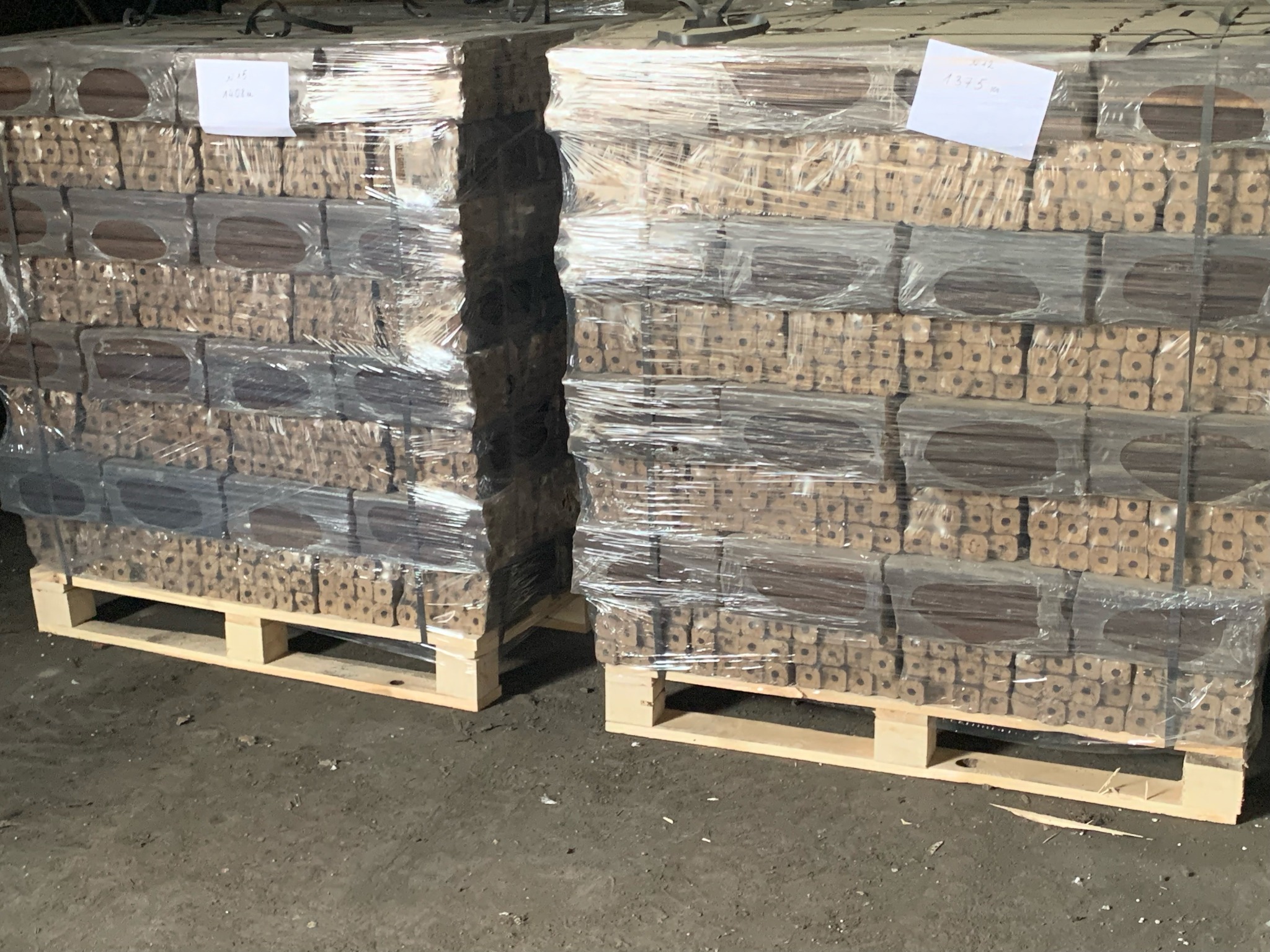 Dwa palety z brykietem drzewnym owinięte folią stretch, widoczne etykiety z informacjami o wadze na wierzchu palet.