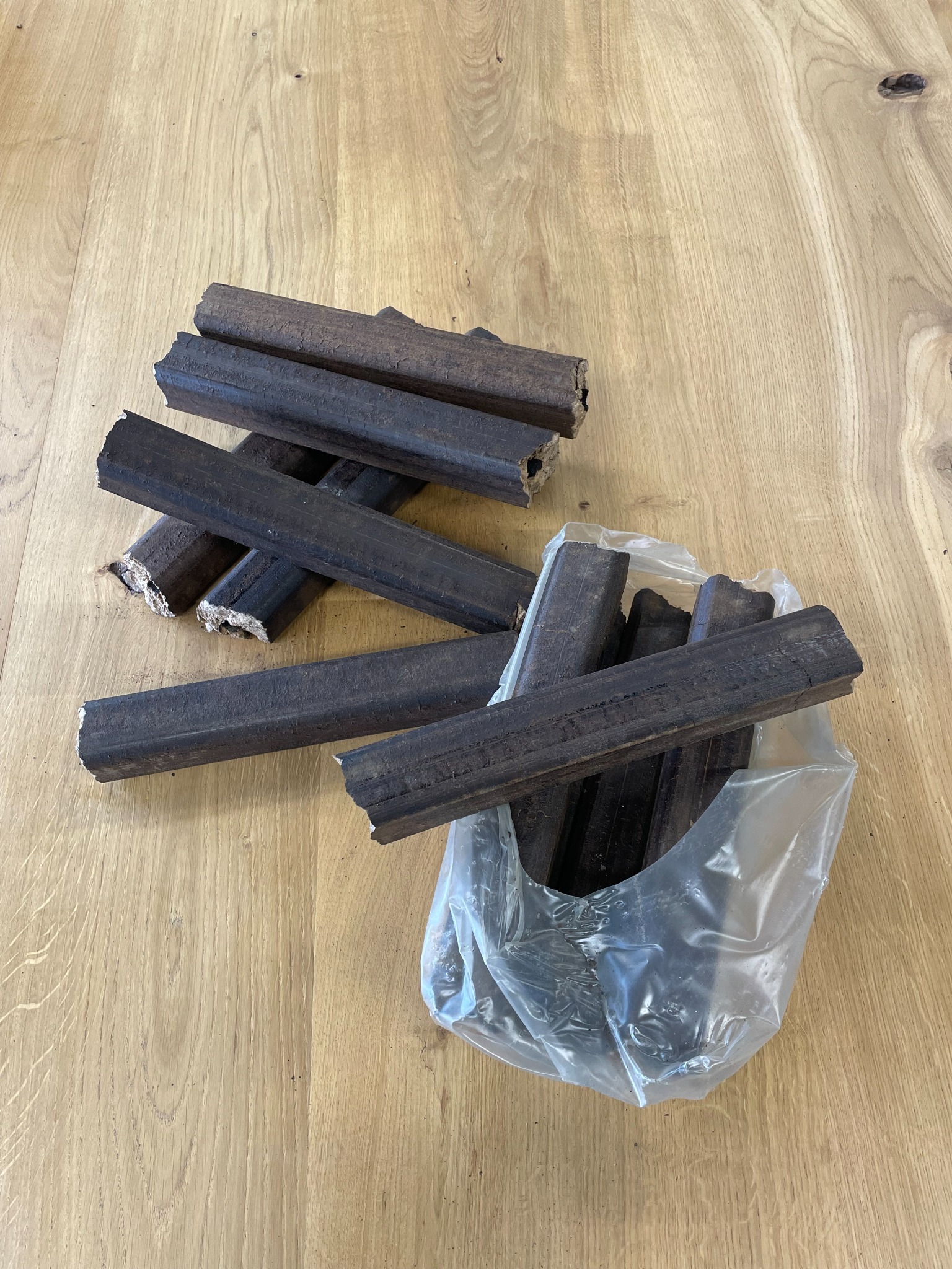 Brykiet drzewny w przezroczystej folii i ułożony obok na drewnianym blacie z widocznym uszczerbkiem na jednym z kawałków.