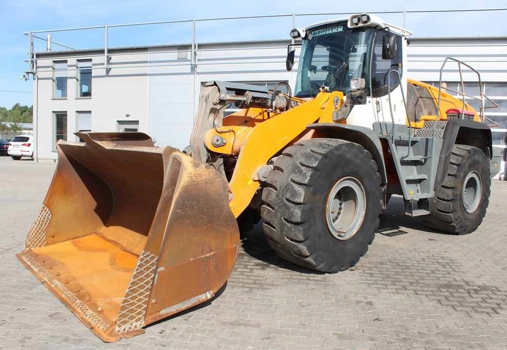 Żółto-biała ładowarka kołowa marki Liebherr stoi na placu z kostki brukowej, z widocznym dużym, rdzawym łyżką i masywnymi oponami.