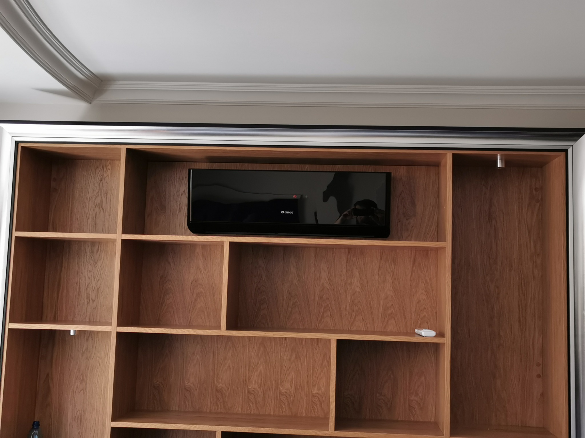 Wbudowana drewniana szafa z półkami i zamontowanym klimatyzatorem marki Gree, widoczny pilot na jednej z półek.