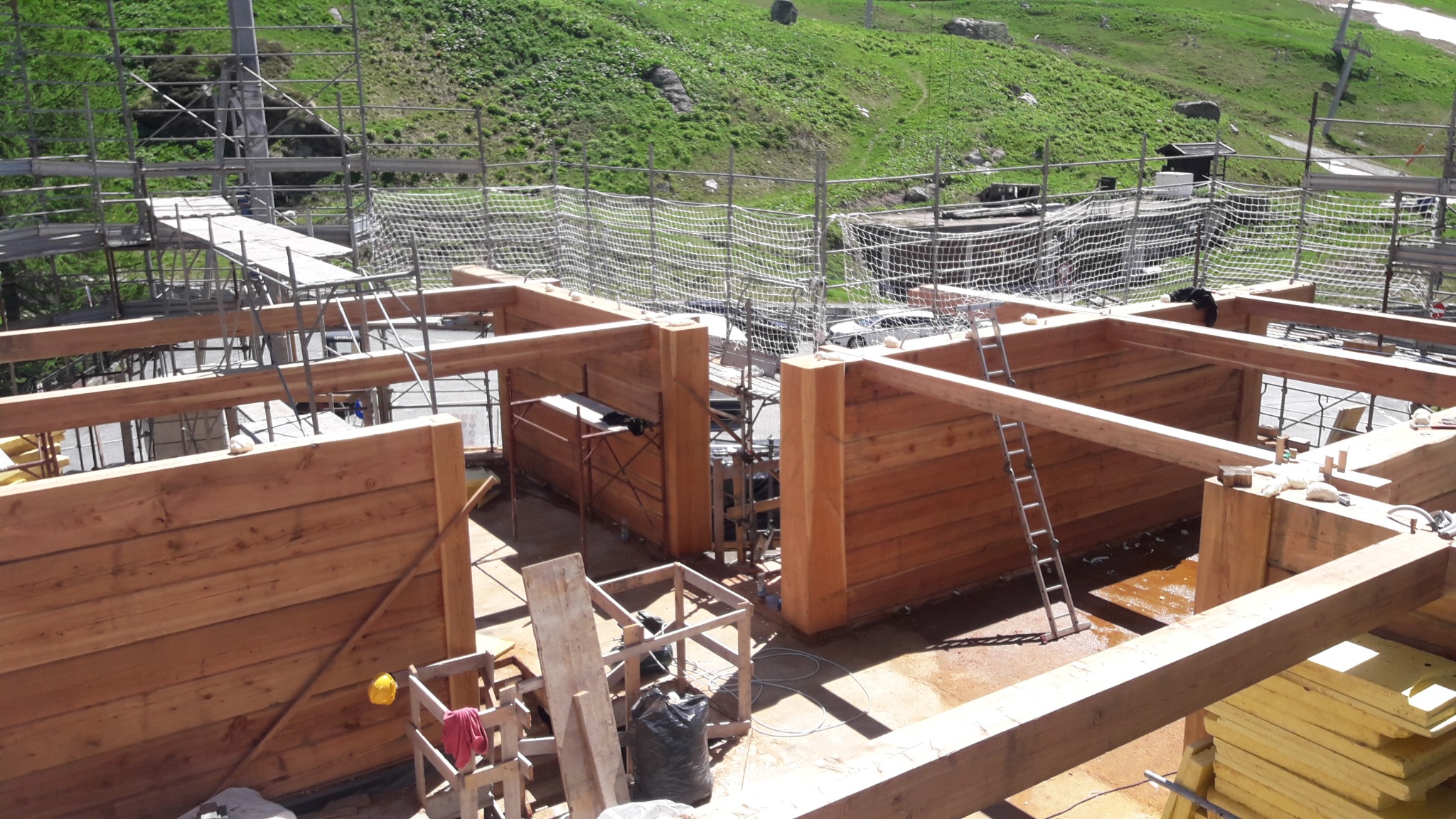 Konstrukcja domu z bali 40cm z modrzewia włoskiego w trakcie budowy, widoczne rusztowania i otoczenie zielonych wzgórz.