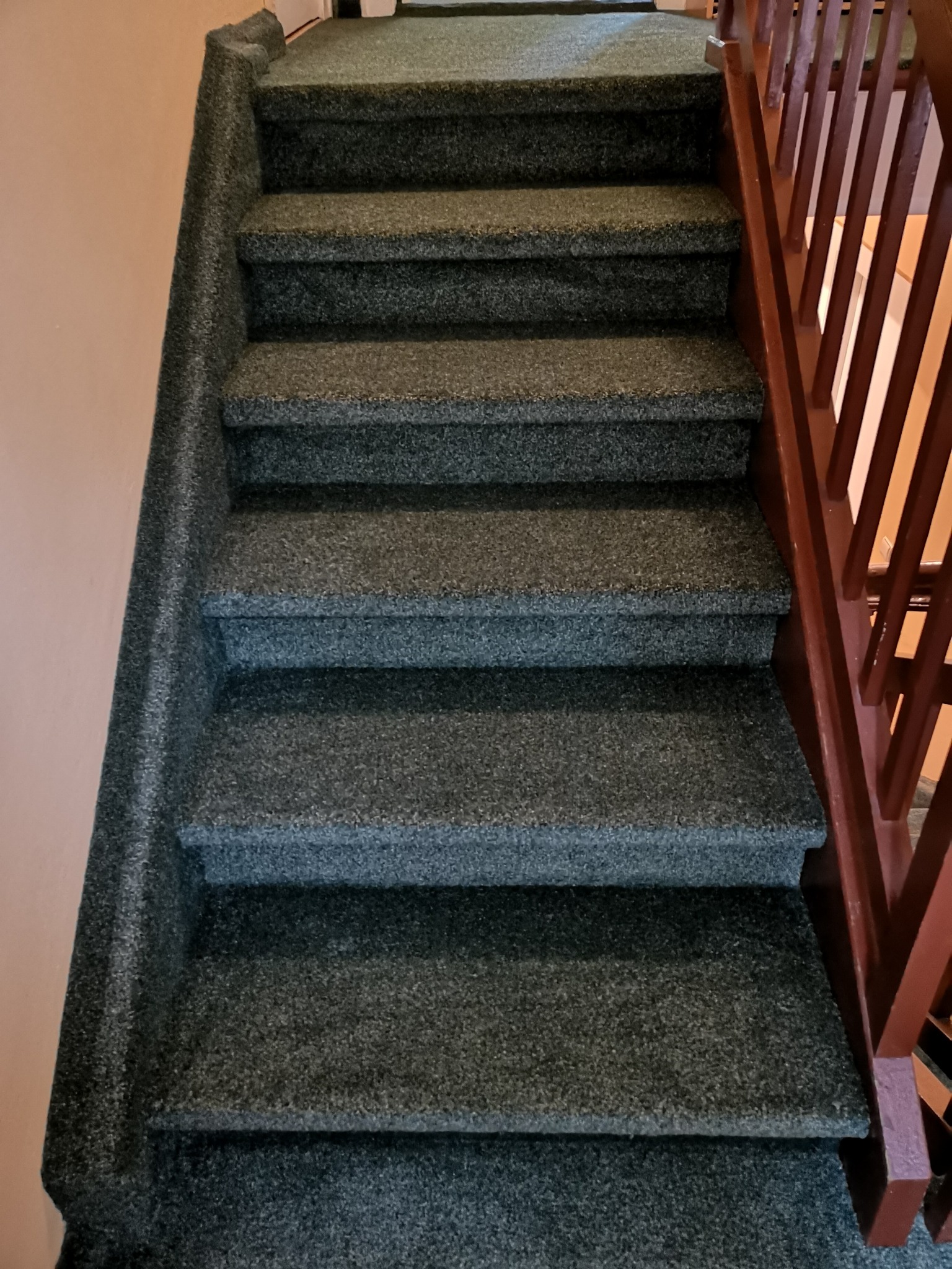 Schody pokryte ciemnoszarą wykładziną dywanową, widoczne brązowe drewniane poręcze