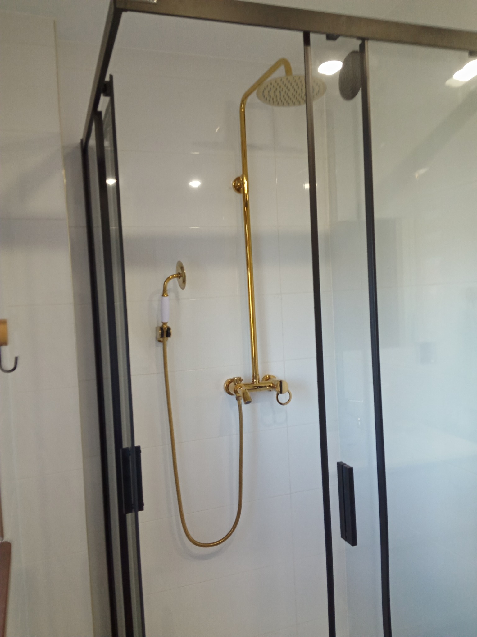 Nowoczesna kabina prysznicowa z czarnymi profilami i złotą armaturą retro, białe płytki na ścianach.