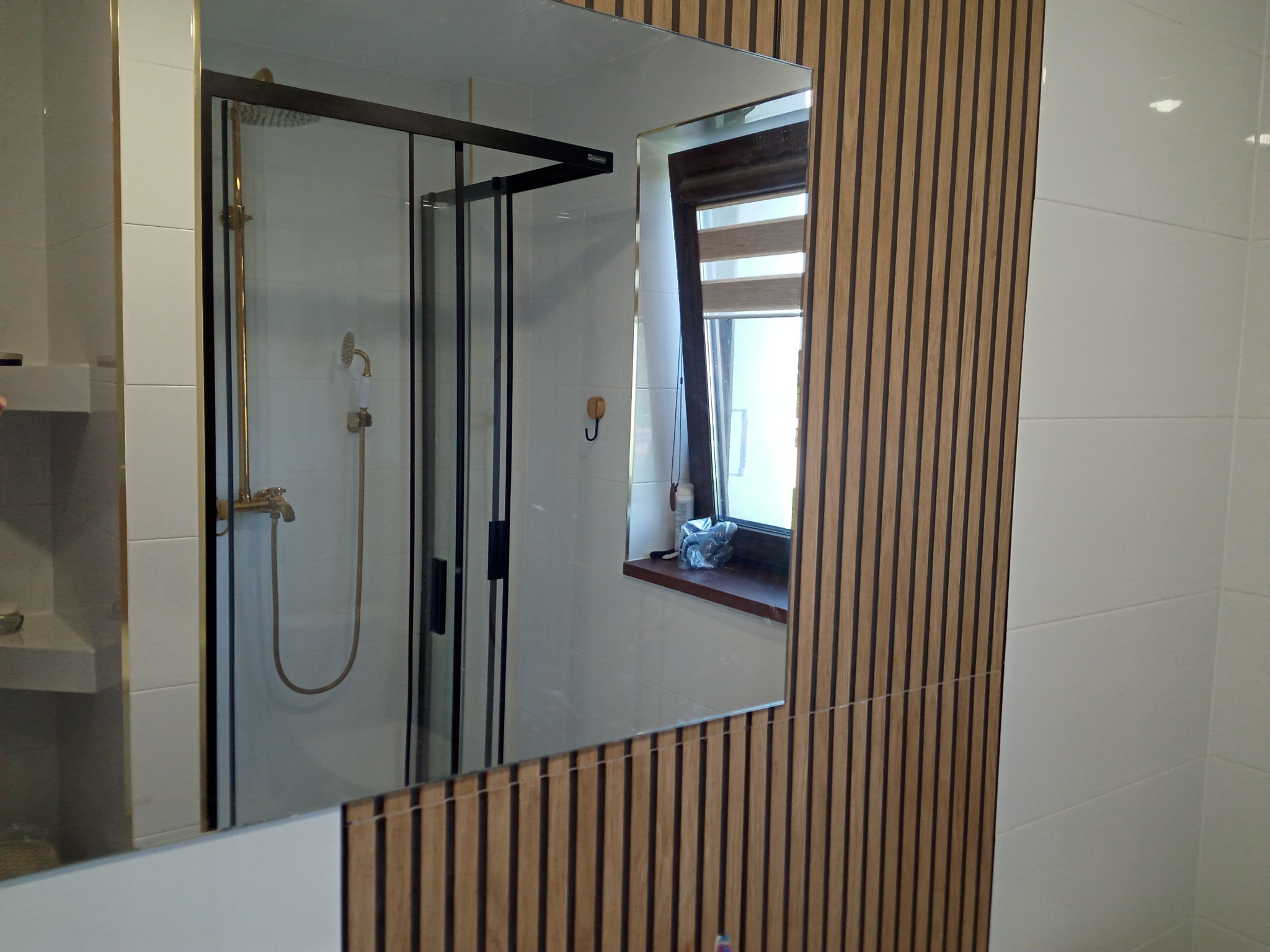 Nowoczesna łazienka z kabiną prysznicową w kolorze czarnym, widoczna w lustrze, obok ściana z drewnianych paneli dekoracyjnych.