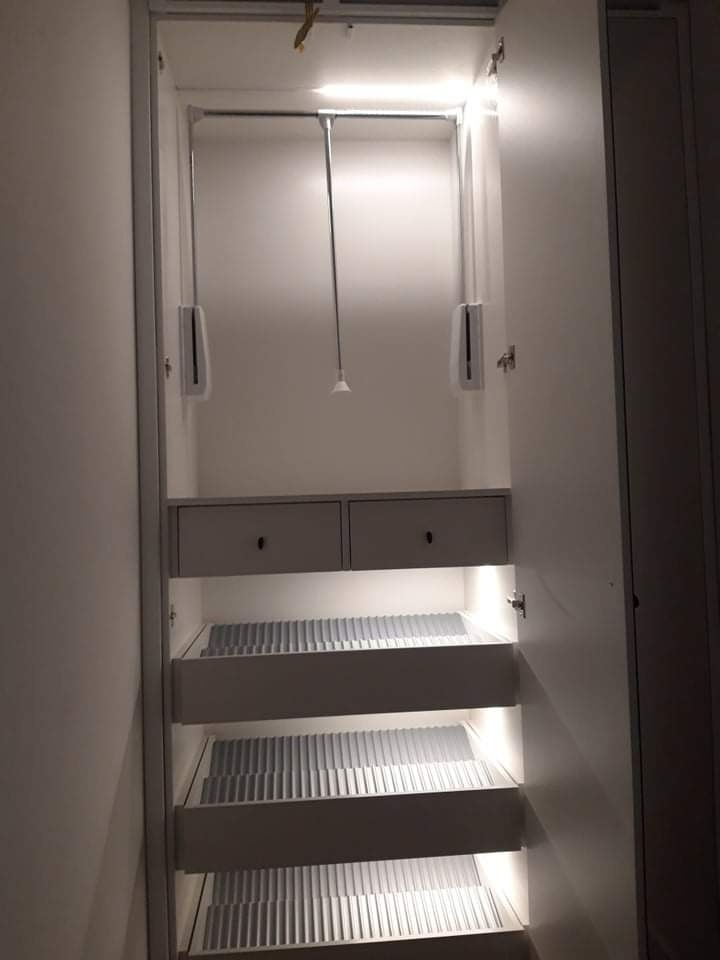 Wnętrze białej szafy wnękowej z szufladami i drążkami, oświetlenie LED podkreśla nowoczesny design.