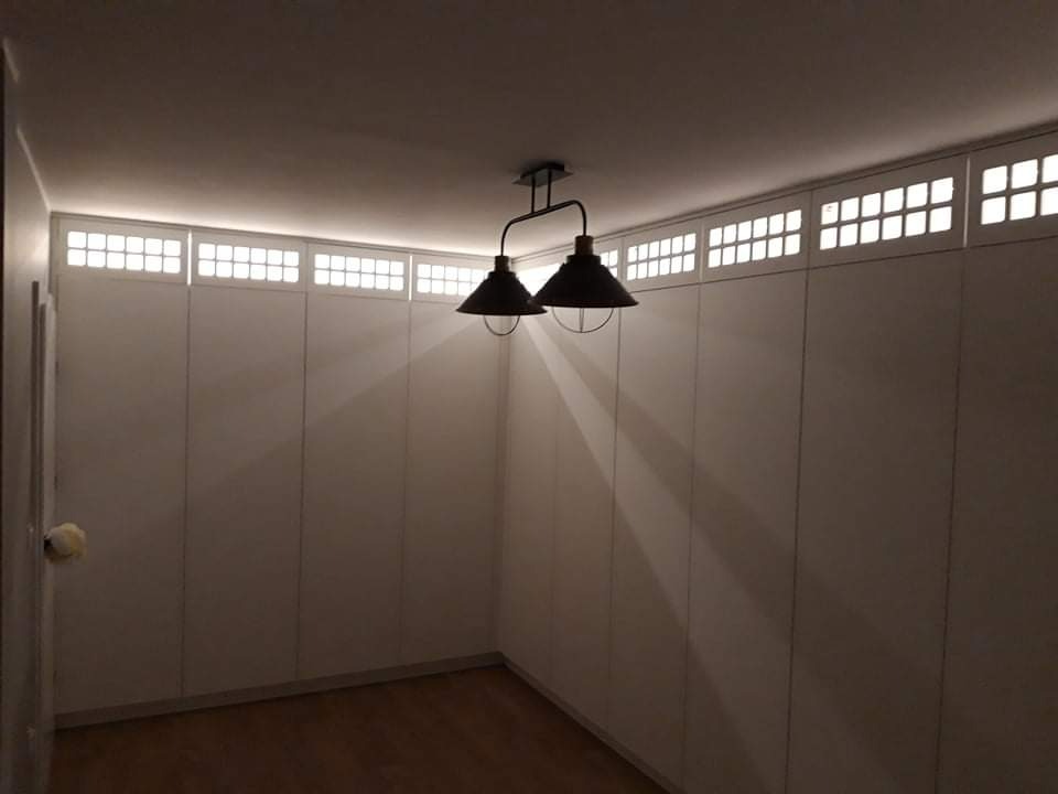 Białe szafy na całej ścianie z górnymi panelami z podświetlanymi kwadratami, oświetlone przez dwie lampy wiszące w stylu industrialnym.