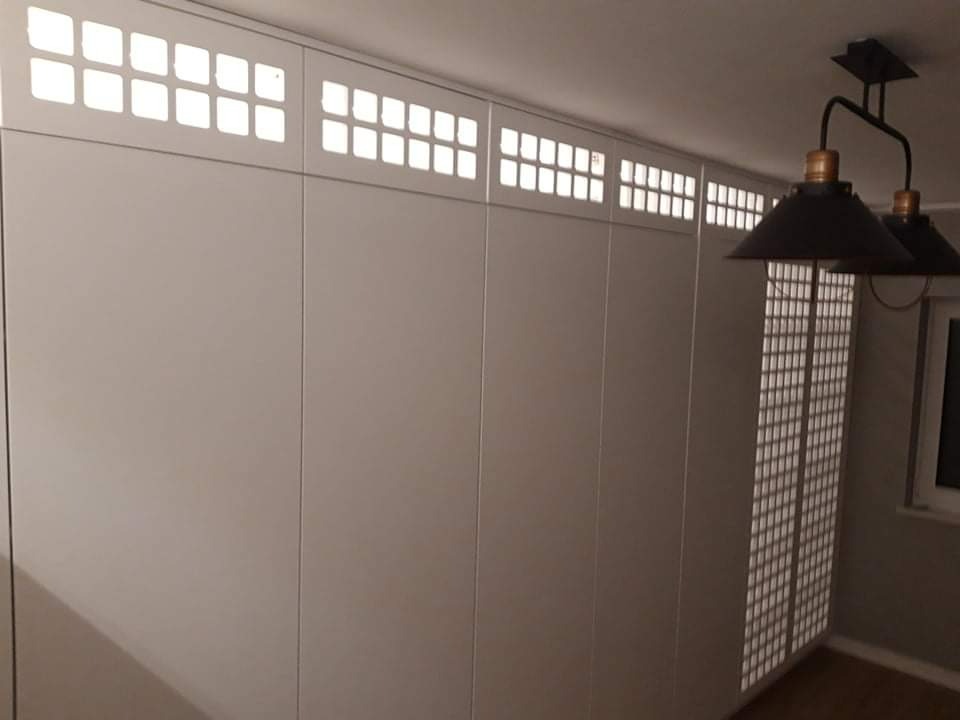 Biała szafa wnękowa z górnymi panelami z podświetlanymi kwadratowymi otworami, widoczna lampa sufitowa w stylu industrialnym.