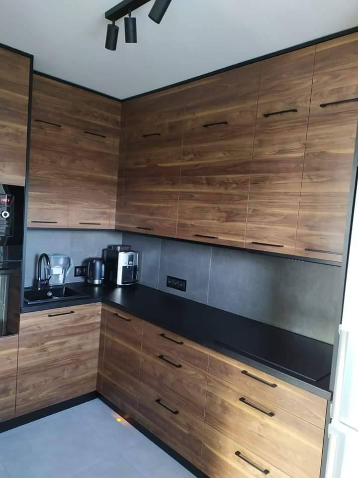 Nowoczesna kuchnia z drewnianymi frontami szafek i czarnym blatem w Trzebnicy, minimalistyczne uchwyty i oświetlenie punktowe.