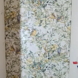 Ułożone płytki ceramiczne z motywem roślinnym i ptaków na ścianie w łazience, widoczne fugi między płytkami.