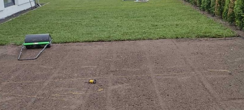 Przygotowany teren pod trawnik z użyciem walca ogrodowego i wytyczonej linki, widoczny fragment położonej trawy w rolkach.