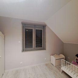 dekoroleta.pl - Pokój dziecięcy na poddaszu z szarymi żaluzjami poziomymi w oknach, białymi meblami i zabawkami na łóżku.