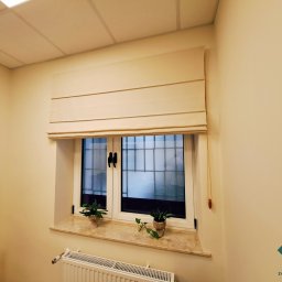 dekoroleta.pl - Kremowa, poziomo składana osłona okienna w pomieszczeniu z białymi ścianami, marmurowym parapetem i dwoma doniczkami z roślinami.