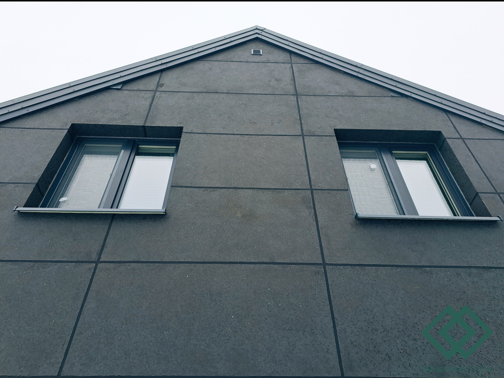 Fasada nowoczesnego domu z dwoma oknami i szarą elewacją w kształcie kwadratów, widok z dołu.