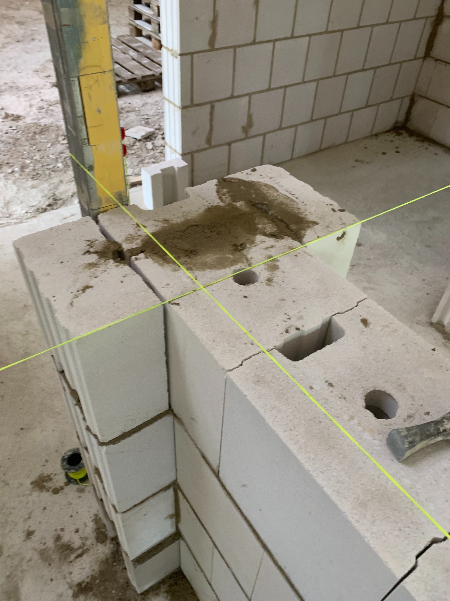 Wznoszenie ściany z bloczków z betonu komórkowego, widoczne naciągnięte sznurki murarskie, zaprawa na bloczkach, młotek murarski obok.