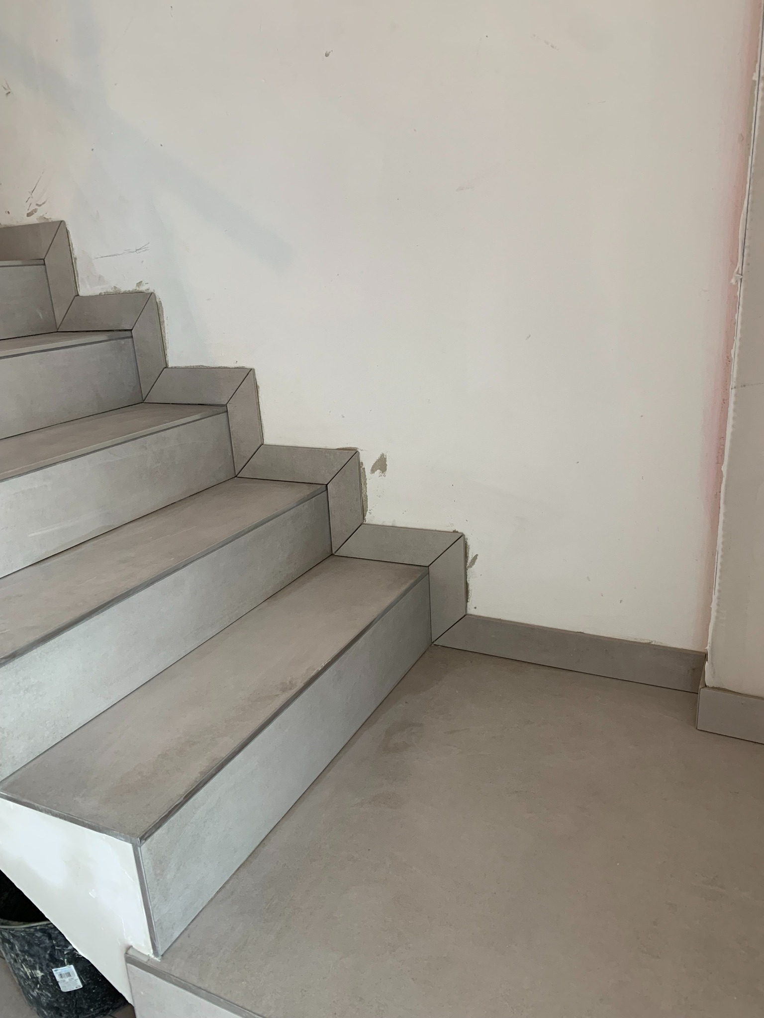 Wykończenie schodów płytkami w szarym odcieniu w domu w Zagórowie, widoczne niedoskonałości na ścianie wskazują na trwający remont.