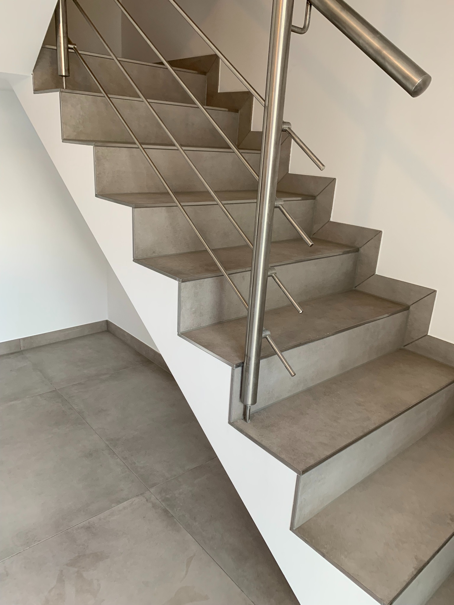 Schody wewnętrzne wykończone szarą płytką gresową, z metalową balustradą o minimalistycznym designie, widok z dołu na tle białych ścian.