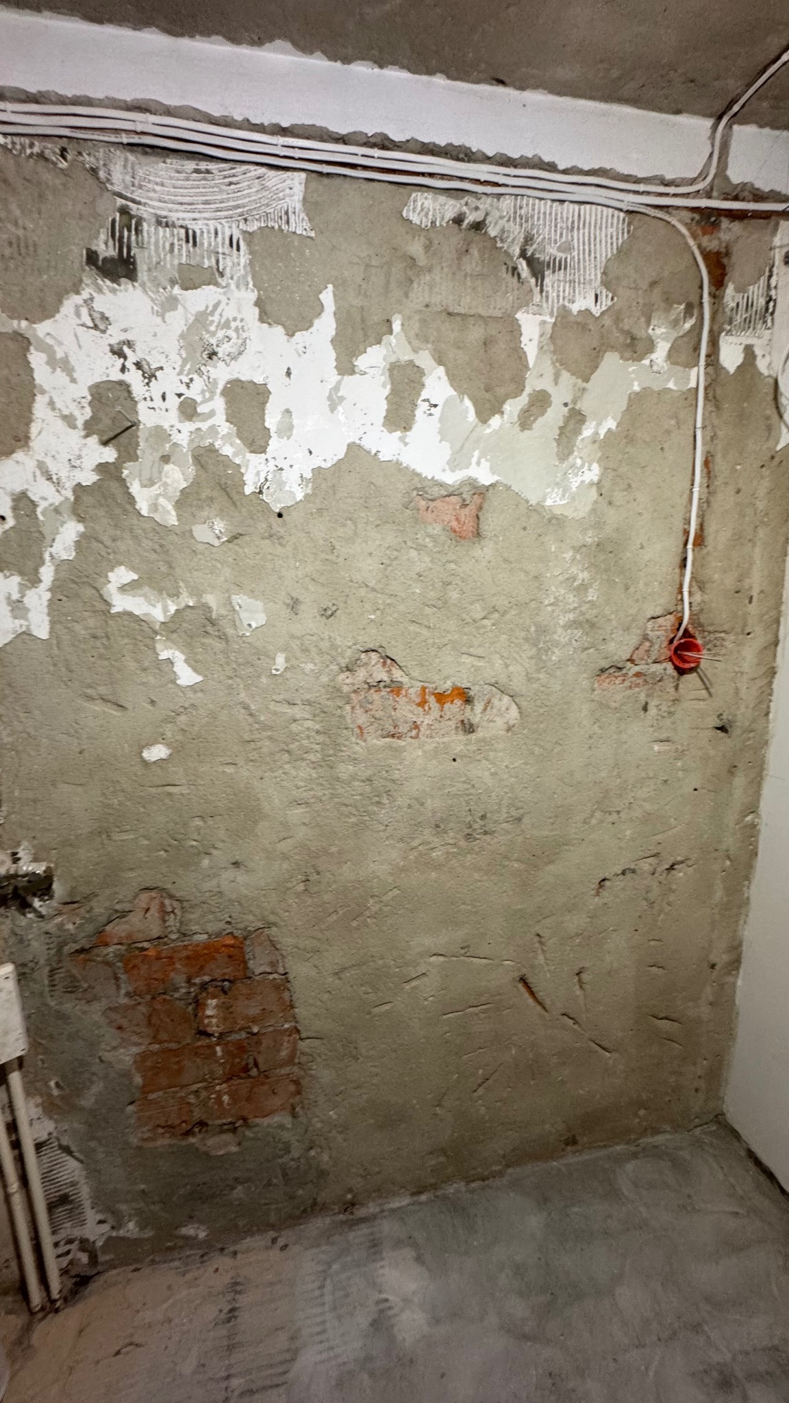 Ściana w trakcie skuwania tynku, z widocznymi fragmentami cegieł i instalacją elektryczną. Przygotowanie do remontu, surowy stan wnętrza.