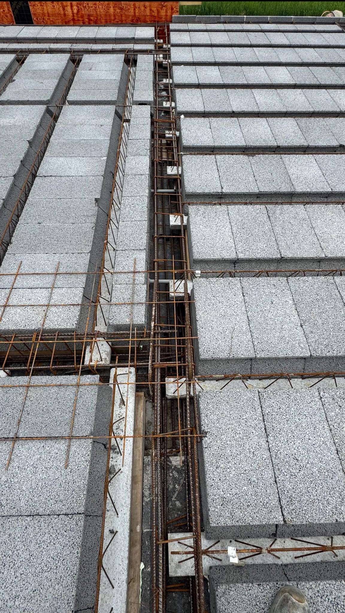 Szare bloczki stropowe zbrojone stalą, widok z góry. Przygotowanie do zalewania betonem. Detal zbrojenia w szalunku. Budowa stropu Teriva.