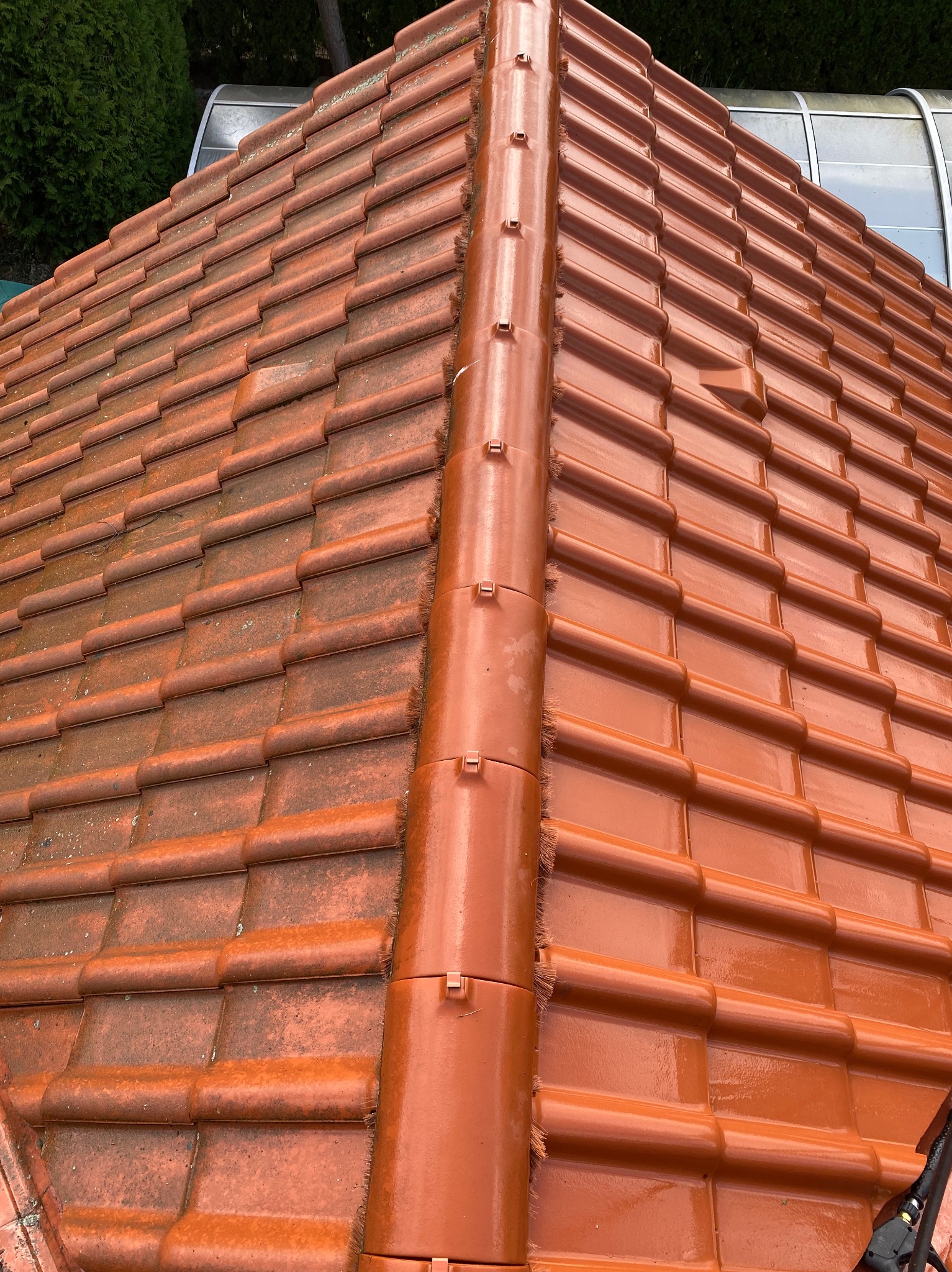 Częściowo umyty dach z czerwonej dachówki, widoczna różnica w czystości. Po lewej stronie dachówka jest czysta i błyszcząca, po prawej brudna i matowa. Centralnie rynna.