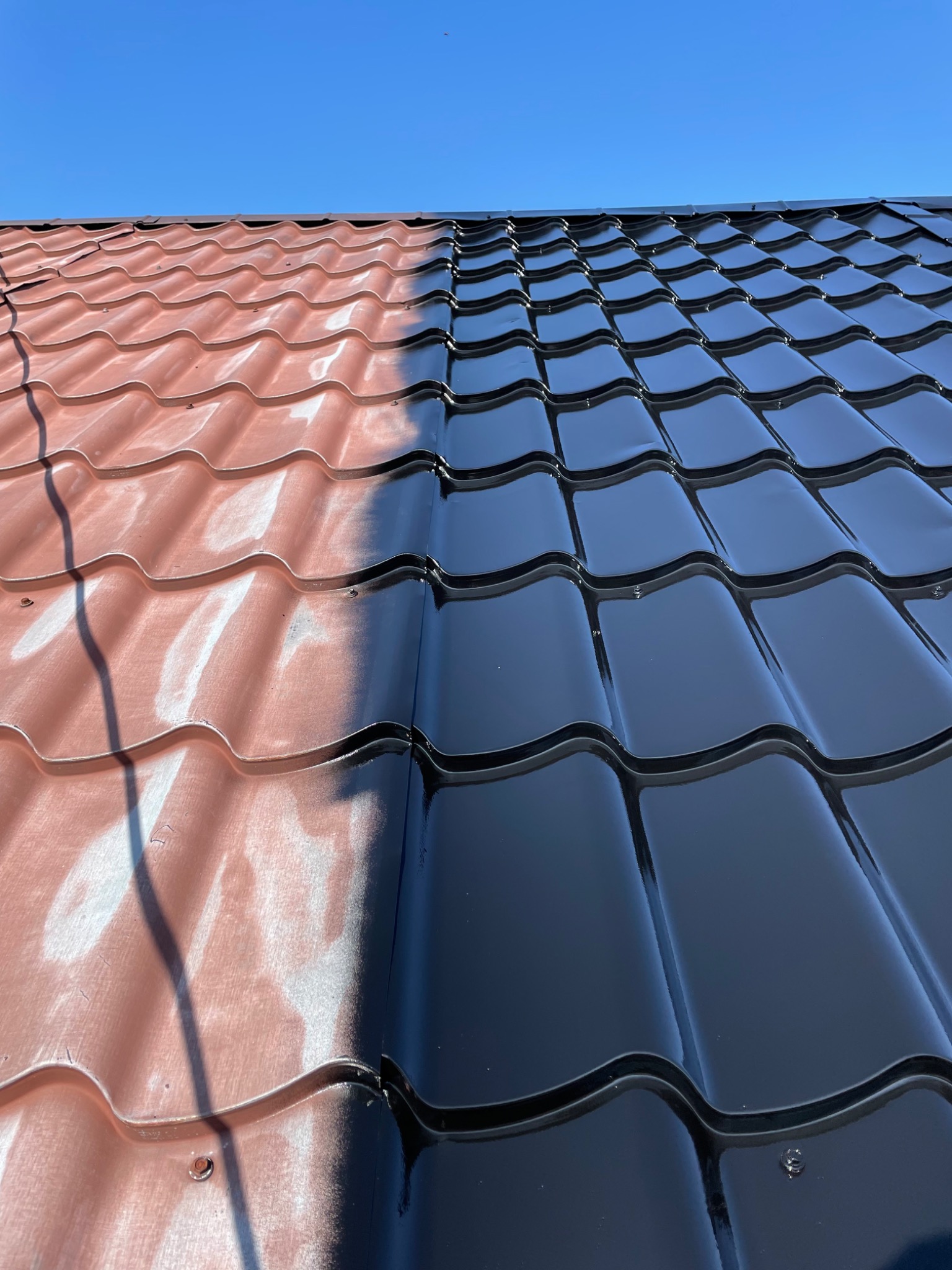 Częściowo umyty dach z blachodachówki, widoczna różnica między brudną a czystą powierzchnią pod błękitnym niebem.