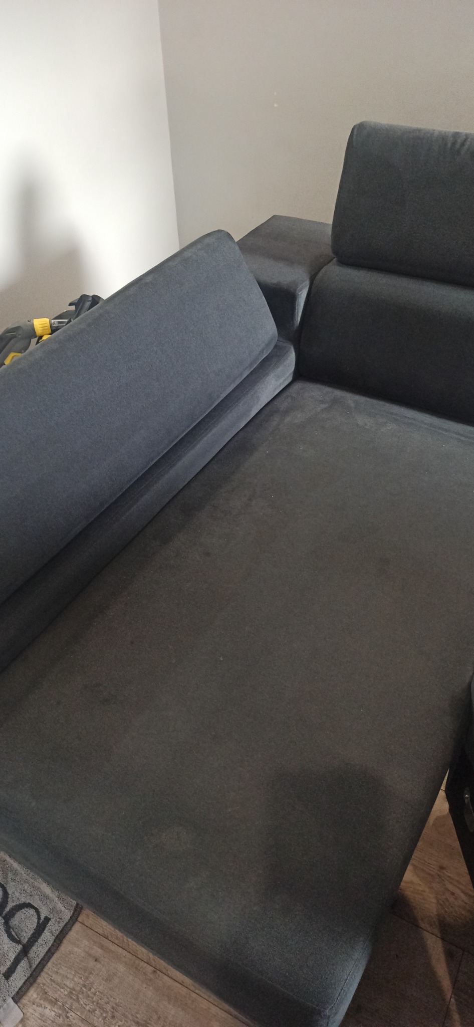 Szara, narożna kanapa po praniu tapicerki w Bytomiu, widoczne delikatne ślady po plamach, jasne tło ściany.