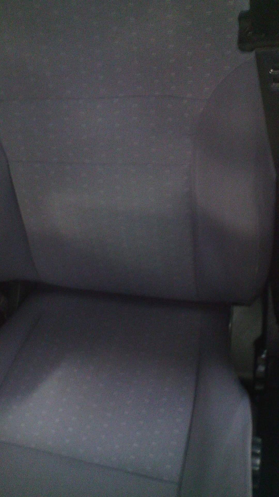 Szare, teksturowane siedzenie samochodowe z widocznym zagłówkiem i bocznym oparciem, sfotografowane z bliska w słabym oświetleniu.