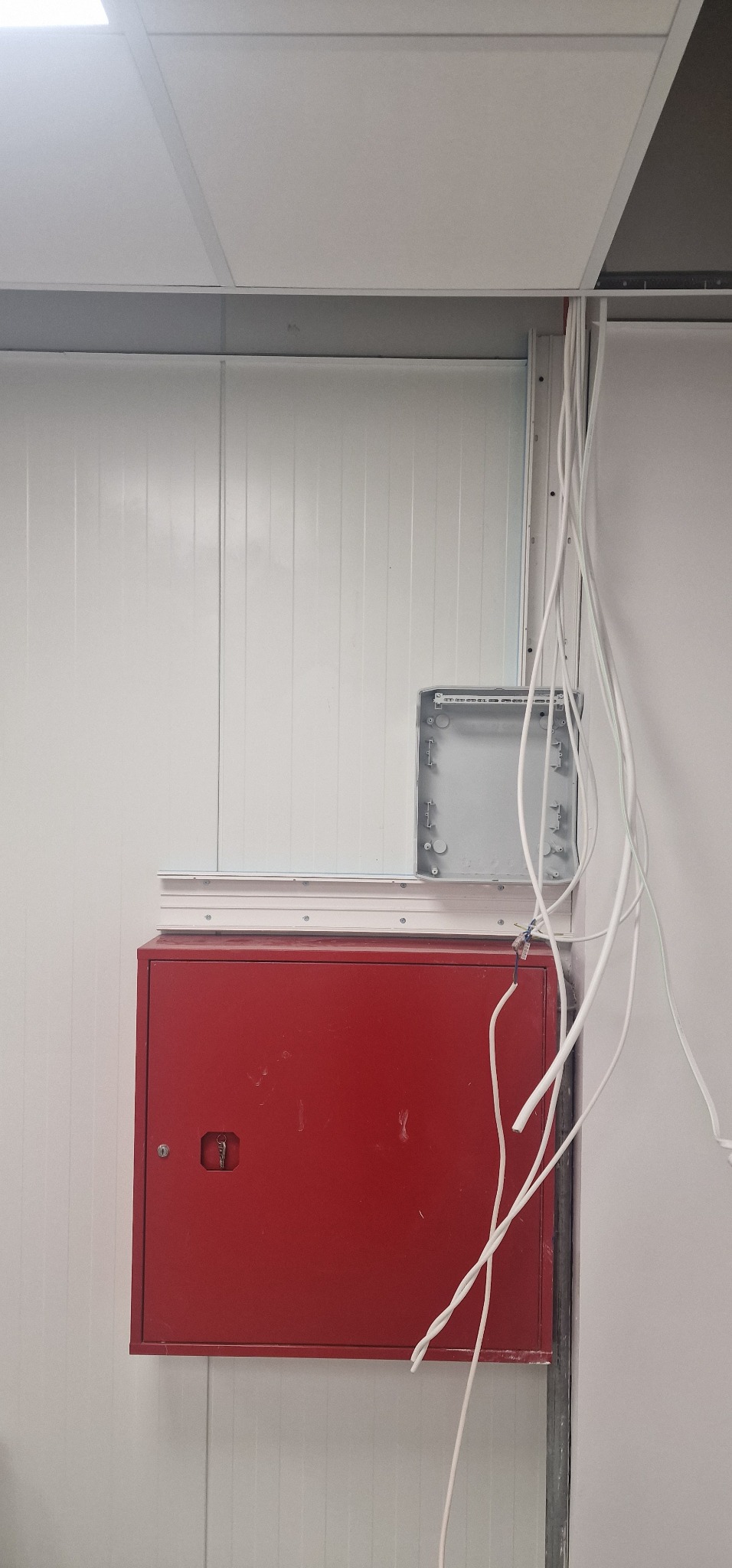 Czerwona szafka elektryczna z wystającymi przewodami w trakcie montażu instalacji w Ostrołęce, widoczne puszki instalacyjne i kable prowadzone wzdłuż ściany.