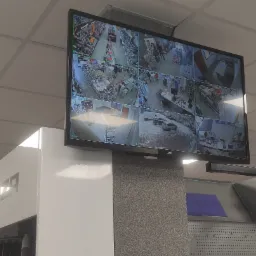 Ekran monitoringu JVC z podglądem z wielu kamer w sklepie, widoczne regały z farbami, narzędziami i klientami, data i godzina na ekranie.