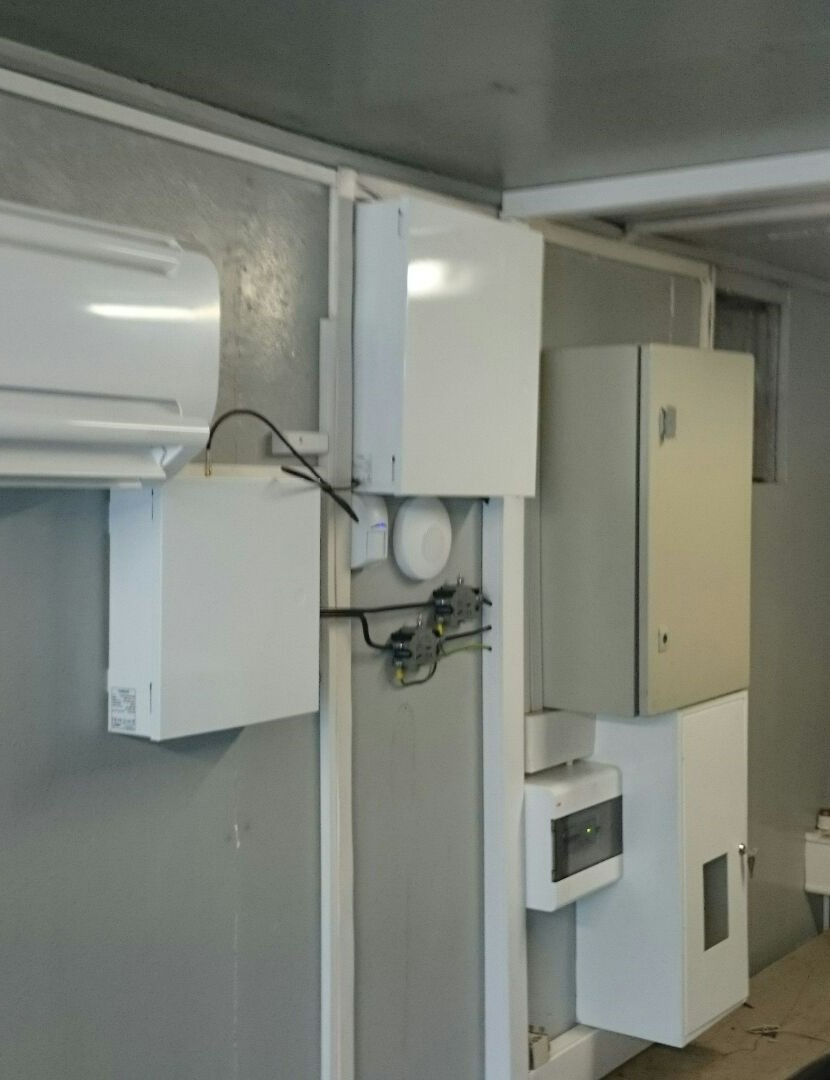 Wewnętrzna instalacja elektryczna z licznymi białymi skrzynkami, przewodami i czujnikiem ruchu na szarej ścianie w pomieszczeniu.