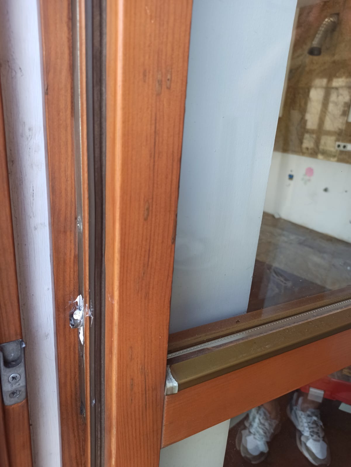 Detail uszkodzonego drewnianego okna z widocznym ubytkiem wypełnionym masą uszczelniającą, z perspektywy wnętrza pomieszczenia w trakcie remontu.