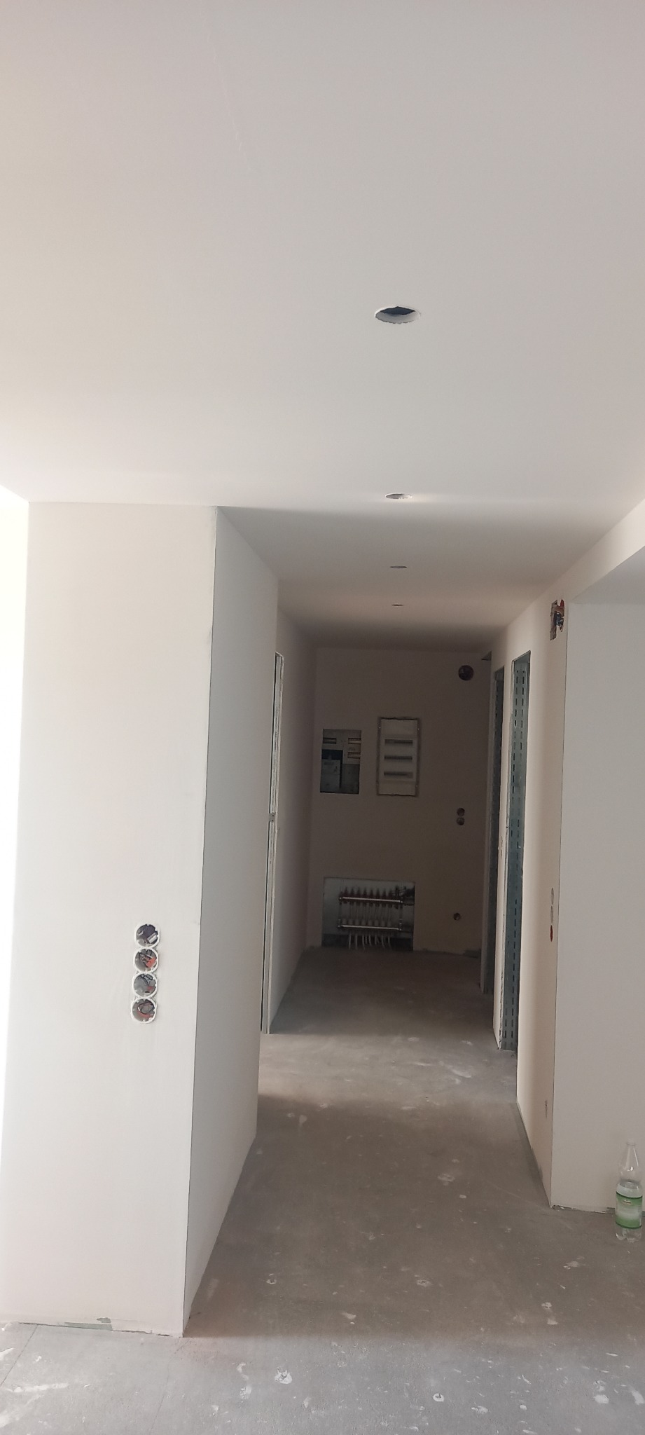 Korytarz w trakcie prac wykończeniowych, widoczne przygotowane otwory na oświetlenie w suficie, puszki elektryczne w ścianie oraz surowa wylewka na podłodze.