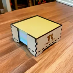 Drewniane pudełko na karteczki biurowe z wygrawerowanym logo firmy, gadżet reklamowy prezentowany w Świętochłowicach na blacie stołu z widoczną strukturą drewna.