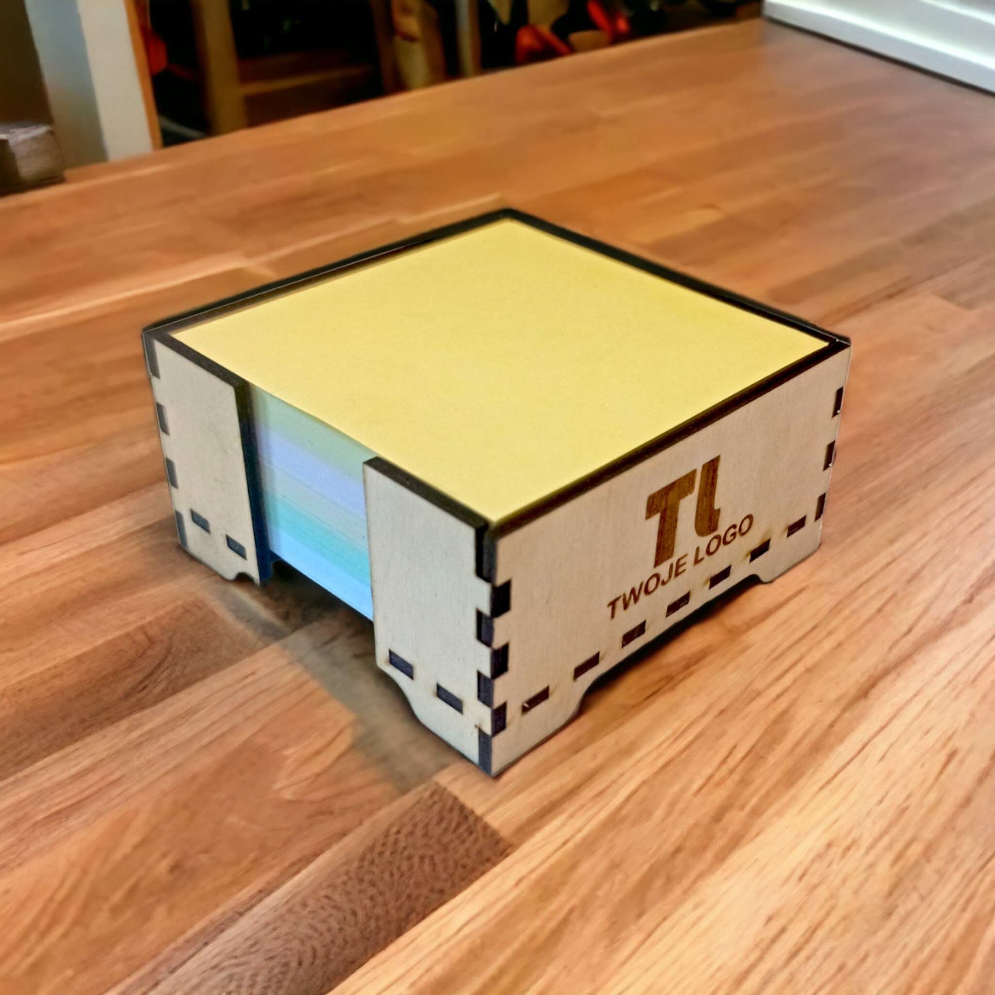 Drewniane pudełko na karteczki biurowe z wygrawerowanym logo firmy, gadżet reklamowy prezentowany w Świętochłowicach na blacie stołu z widoczną strukturą drewna.