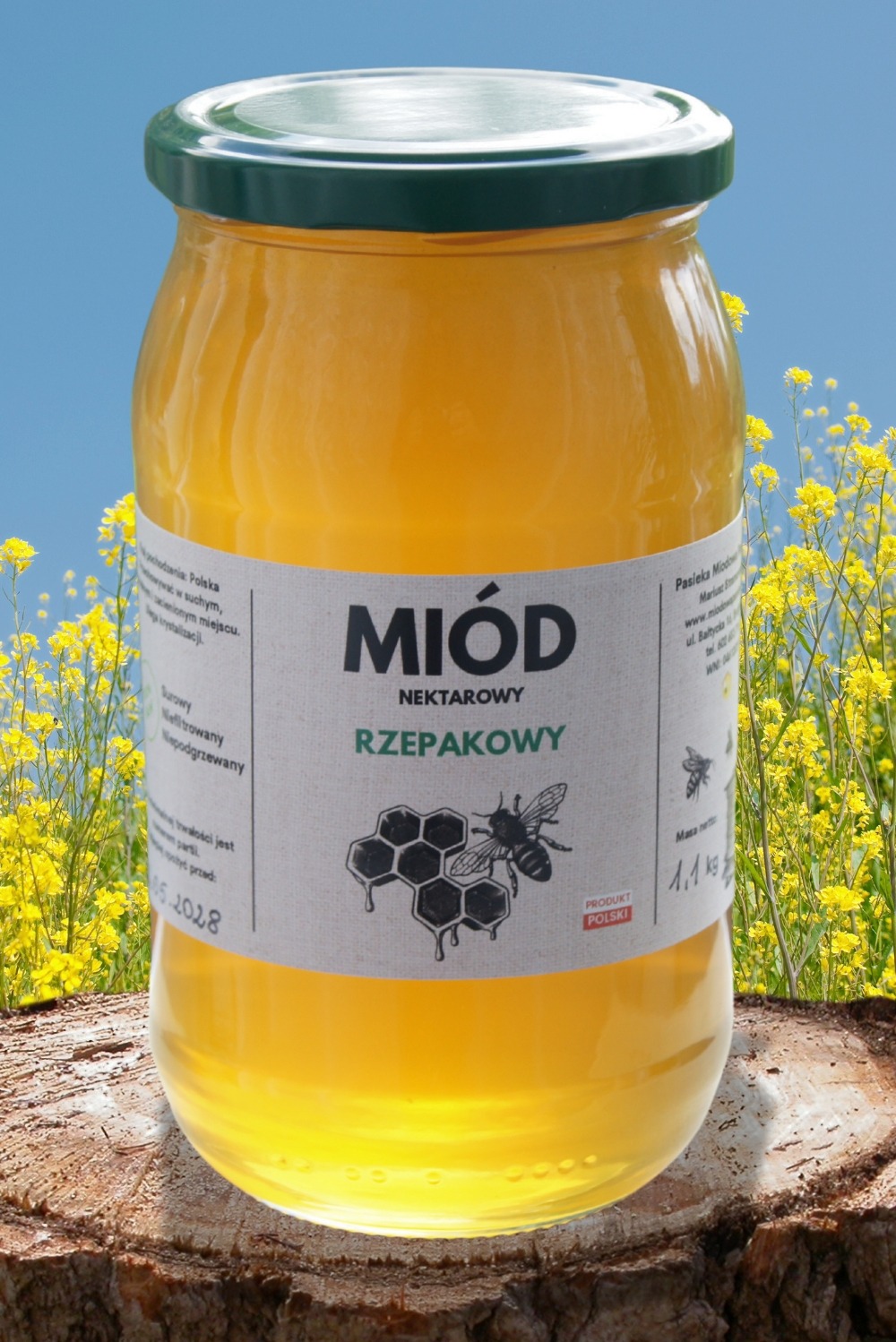 Słoik z miodem rzepakowym na drewnianym pniu, z etykietą prezentującą nazwę i grafikę pszczoły na tle kwitnącego rzepaku i błękitnego nieba.